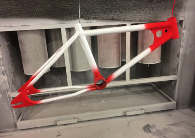 A bicycle frame being spray-painted with a red and white gradient