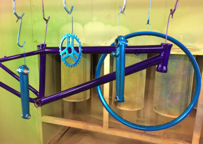 Bicyle parts hanged and painted at Tallaght Powder Coating in purple and metallic cyan