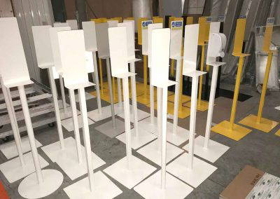 Multiple white and yellow powder coated hand sanitiser stands stacked in workshop Tallaght Powder Coating