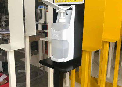 Black powder coated hand sanitiser stand with dispenser in workshop beside white and yellow stands