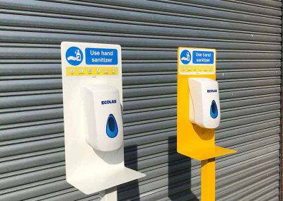 White and yellow powder coated hand sanitiser stands with dispensers outside Tallaght Powder Coating Dublin